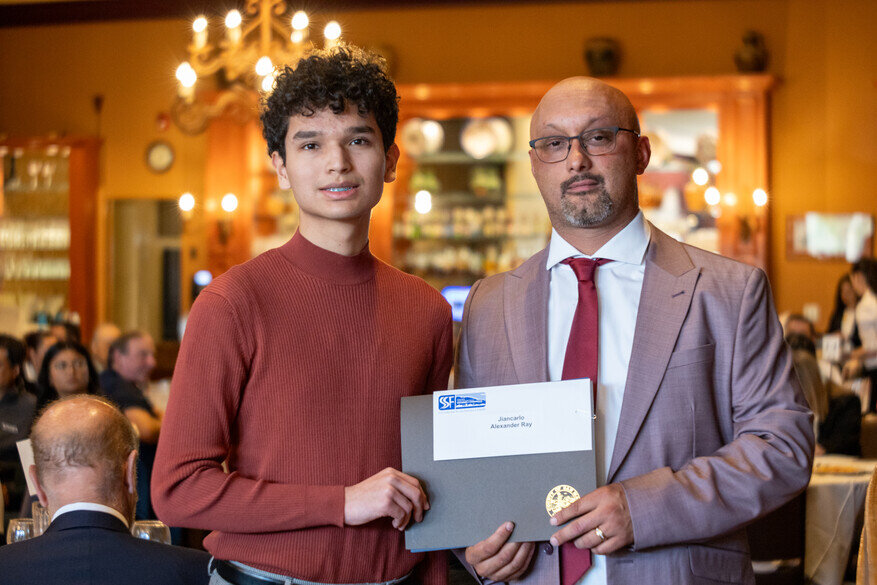a man holding a certificate and a man holding a medal
