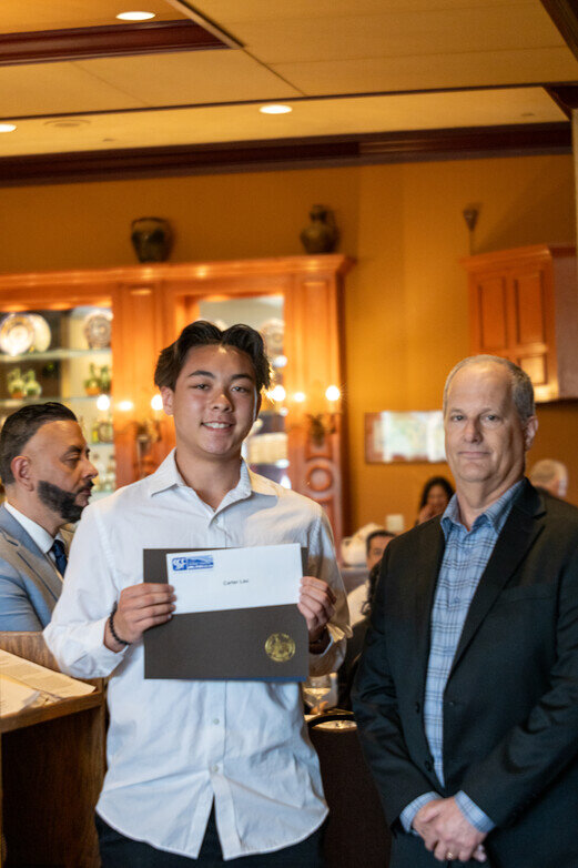 a man holding a certificate and a man standing behind him