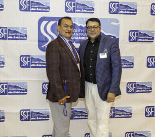 two men standing in front of a white wall with blue and white logos