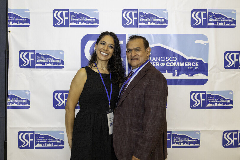 a man and woman standing together in front of a white banner