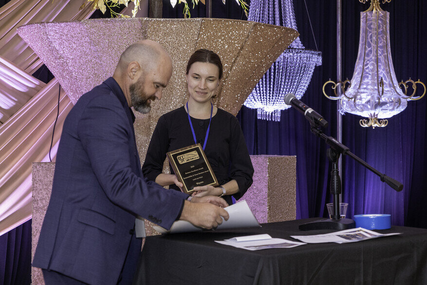 a man and woman standing at a table with a microphone and a plaque
