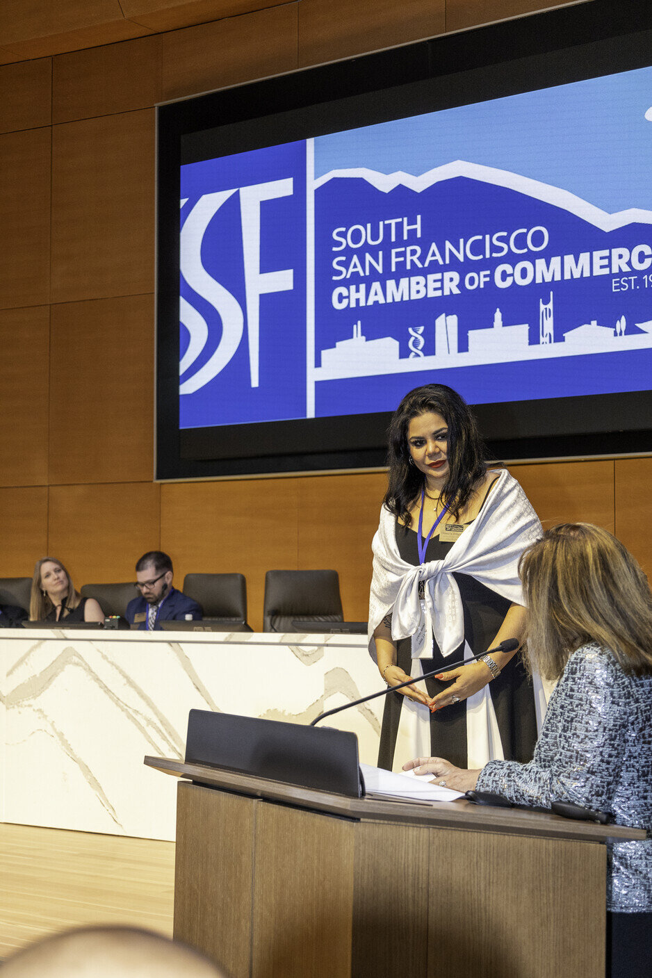 a woman standing at a podium with a large screen behind her